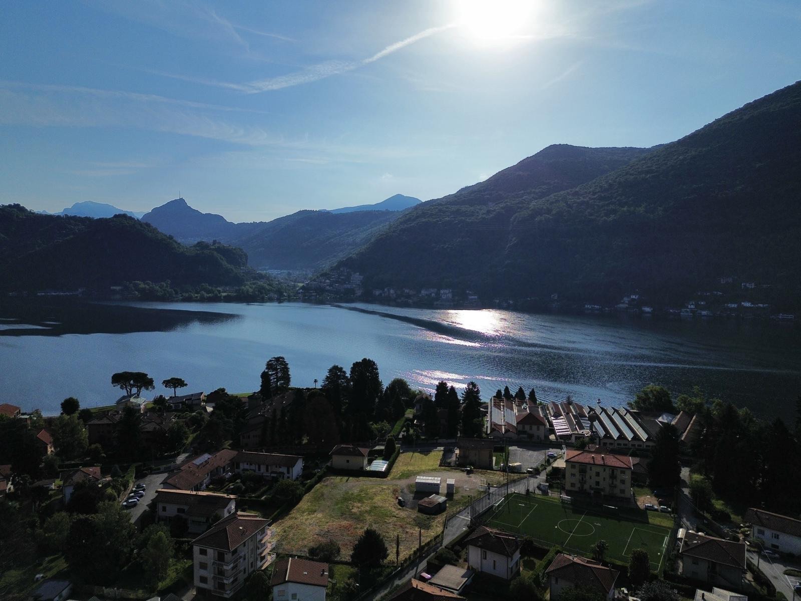 Lake Lugano from above Brusimpiano: the western arm of the lake in the sun, wooded mountains on both shores.