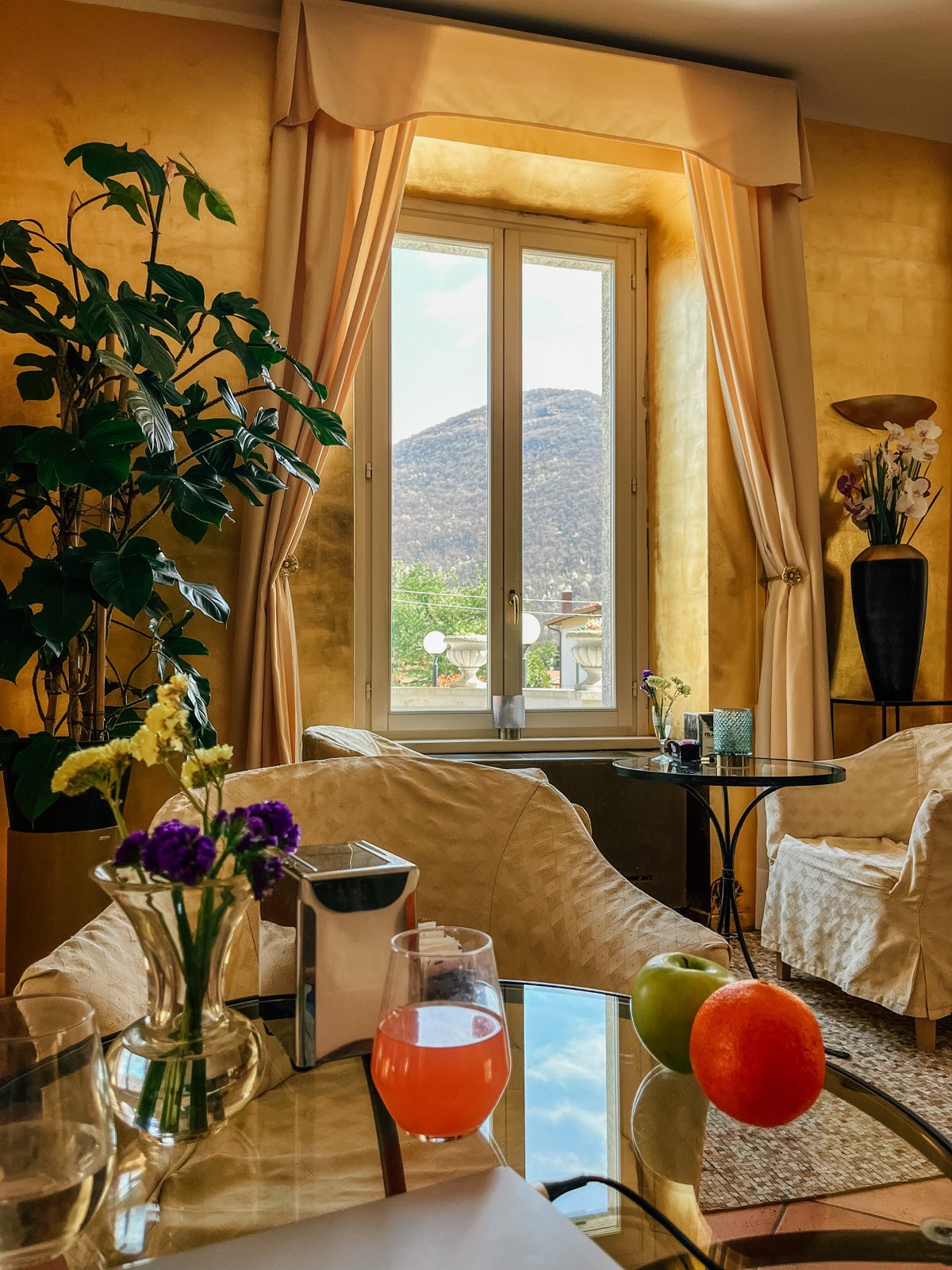A gold-walled relaxation lounge, armchairs, the mountain in the window, fruit and juice.