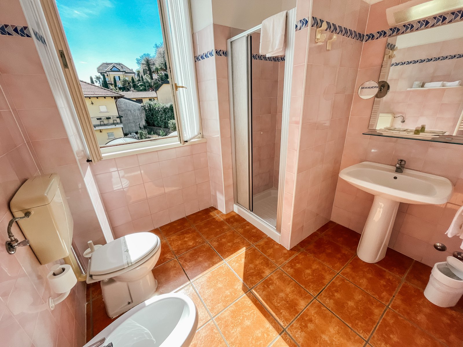 A pink bathroom with a window onto the village.