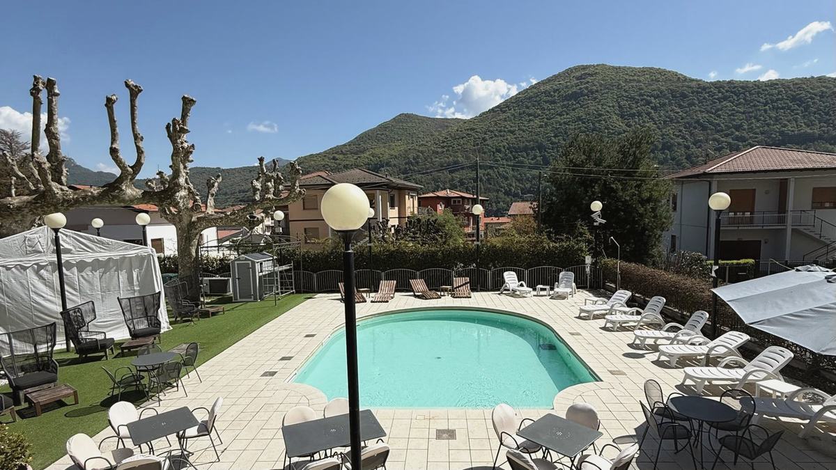 The courtyard pool under a blue sky: loungers, café tables and the wooded mountain behind