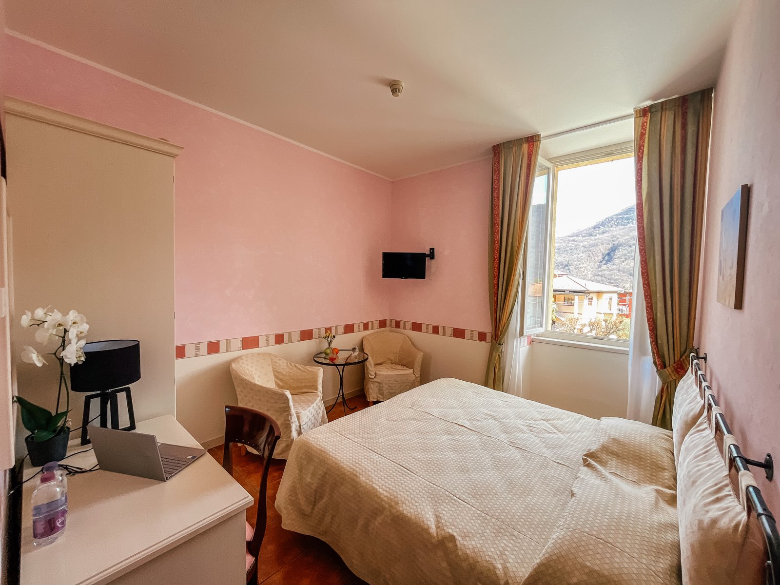 A pink room with a double bed, a window and a small desk.